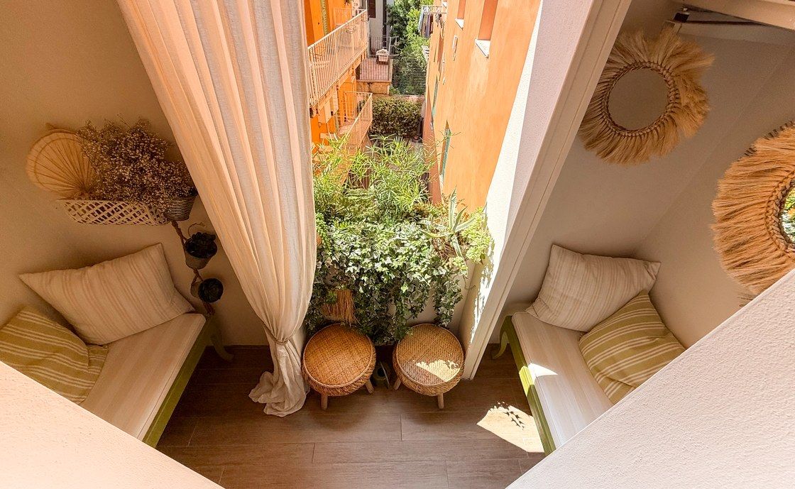 Balkon der Ferienwohnung Madonna del Terraglio mit gepolsterten Bänken, hellem Vorhang und runden Flechtspiegeln