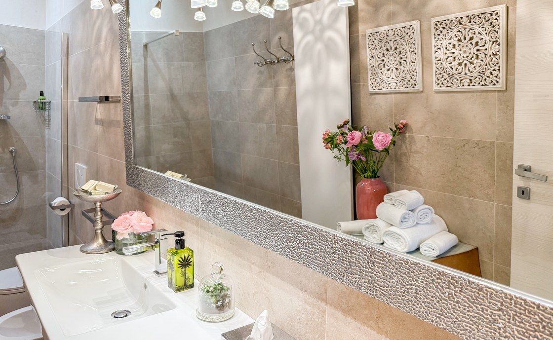 Waschbecken in Santo Stefano unter einem breiten Spiegel mit Mosaikrahmen, mit gerollten Handtüchern und rosa Rosen