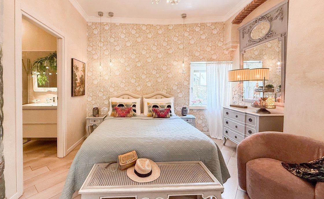 Schlafzimmer in Santo Stefano mit Blumentapete und salbeigrüner Tagesdecke, die Tür zum Bad steht offen