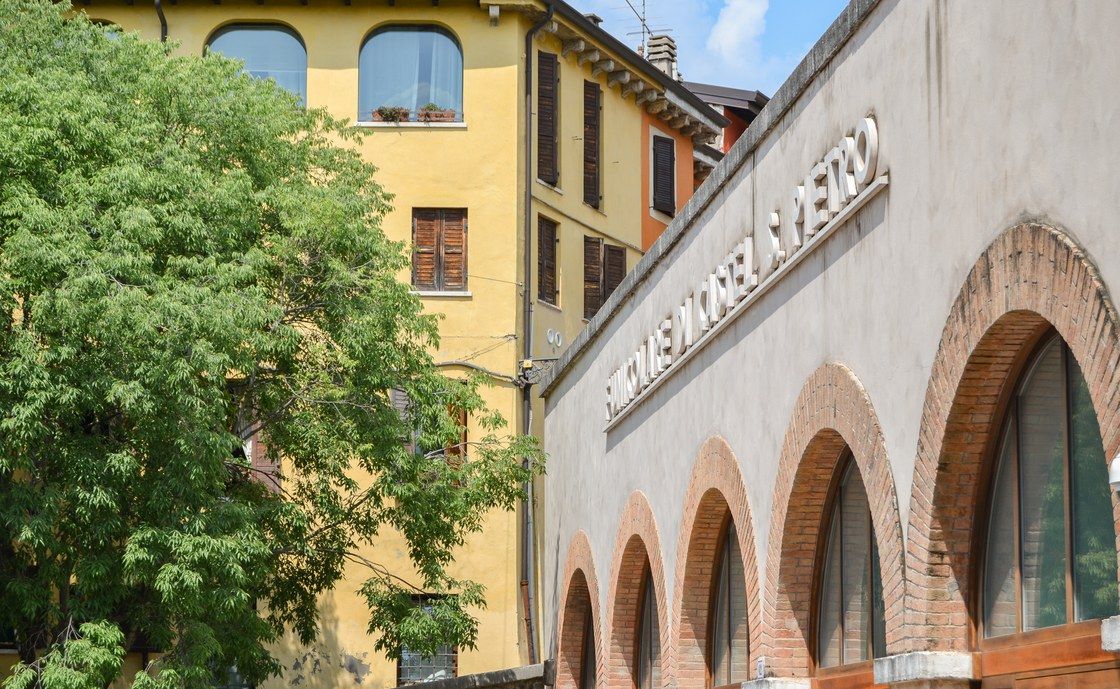 Ockerfarbene Fassade und Backsteinarkade eines Gebäudes in der Altstadt von Verona, zwischen den Bäumen