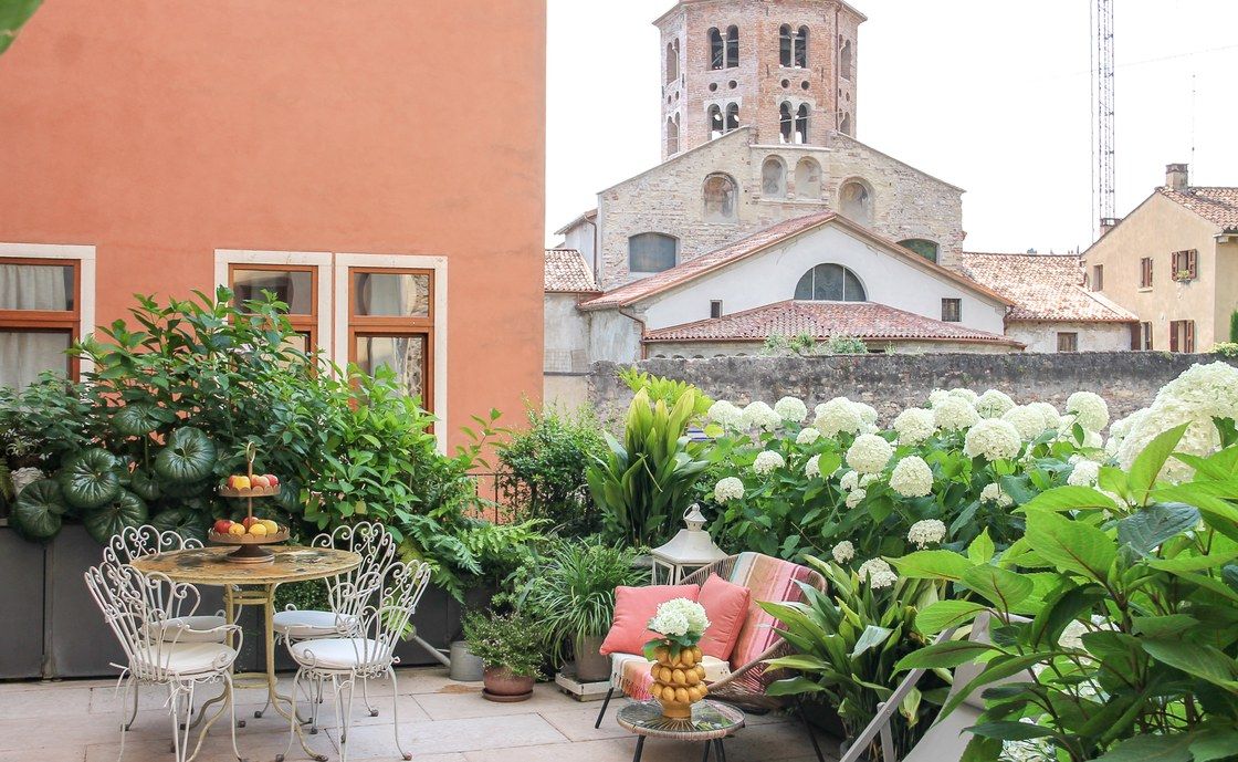 Die private Terrasse von Santo Stefano mit weißem schmiedeeisernem Tisch und Stühlen zwischen Hortensien, unter einem romanischen Glockenturm