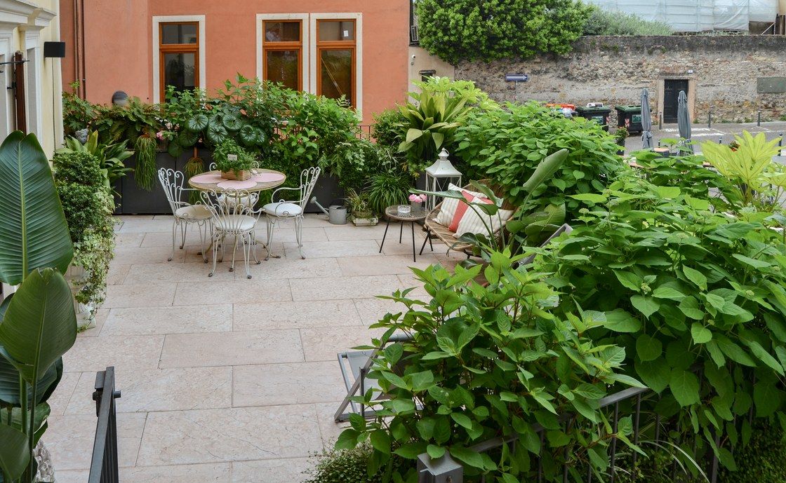 Weite gepflasterte Terrasse in Santo Stefano mit weissem Eisentisch und Stühlen, umgeben von Topfpflanzen