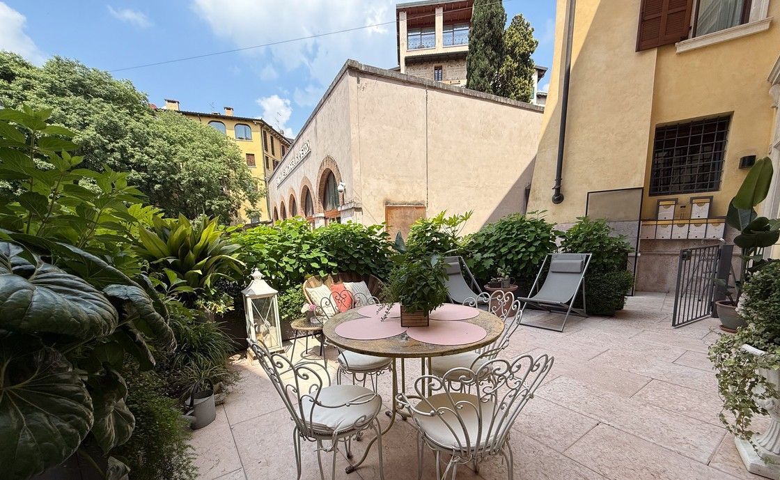 Ampia terrazza pavimentata di Santo Stefano con tavolo e sedie in ferro bianco, circondata da piante in vaso